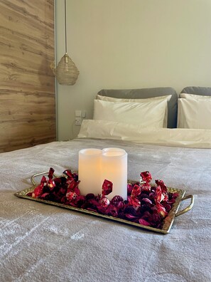 Een bed met witte lakens, een bedlampje en een dienblad met kaarsen en gedroogde bloemen.