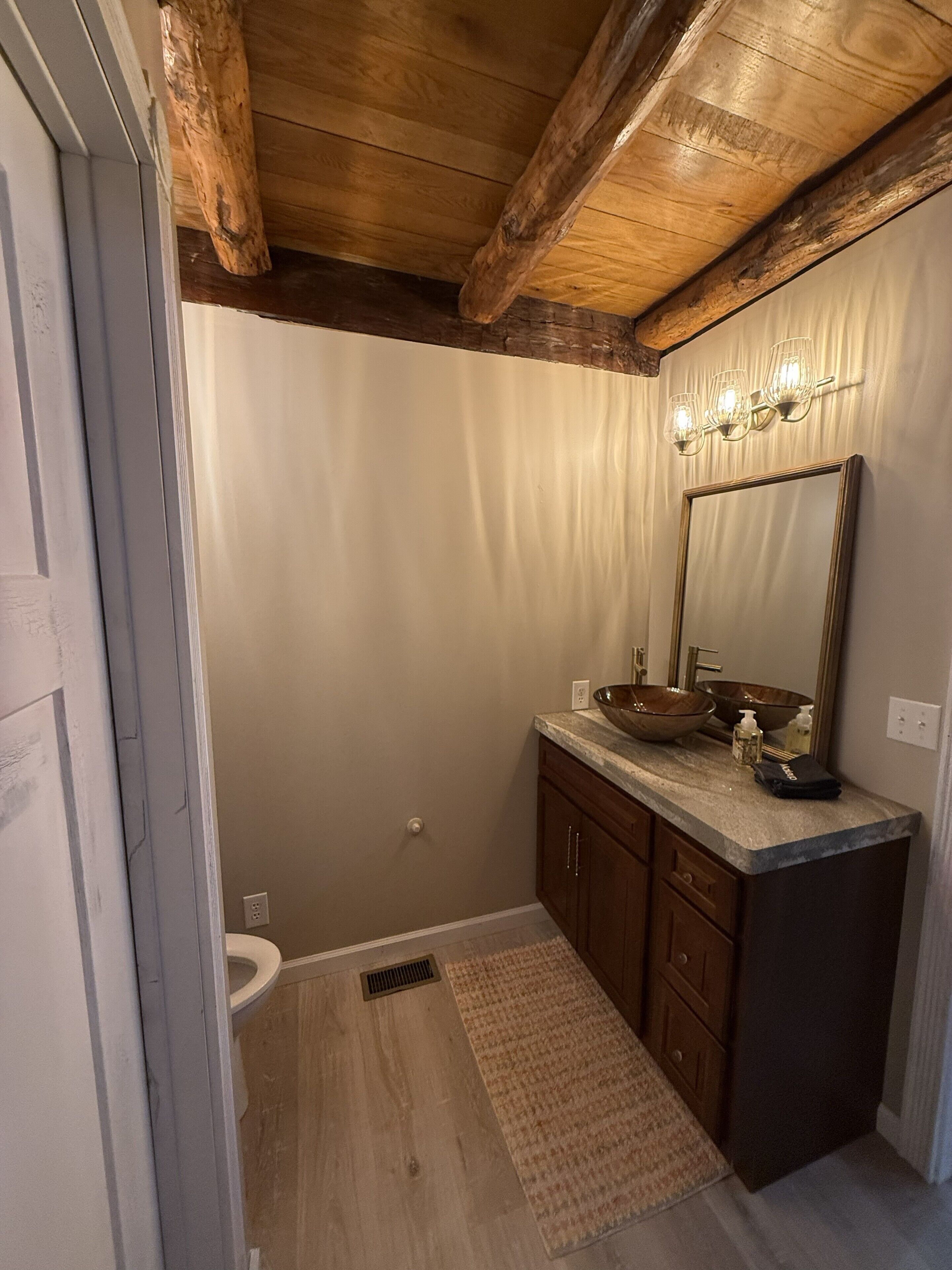 A bathroom with a wooden ceiling, a large mirror, a wooden bowl sink, and a beige rug.