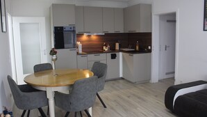 A compact kitchen with modern appliances, a dining area with a round table and chairs, and a sofa in the living area.