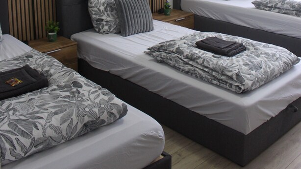A hotel room with three beds, each with a different pillow design, a wooden panel wall, and a ceiling light.