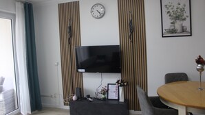 A modern living room with a flat-screen TV, a clock, a framed picture, and a dining table with chairs.