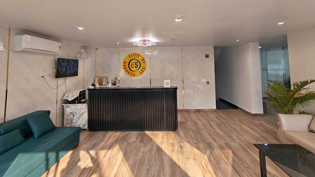 A reception area with a reception desk, a sofa, a TV, and an air conditioning unit. - Hotel Elite One (Gurugram)