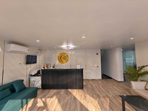 A reception area with a reception desk, a sofa, a TV, and an air conditioning unit.