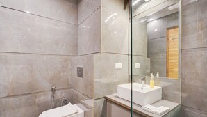 A modern bathroom with a glass partition, a white sink, and a shower area. - Hotel Elite One (Gurugram)