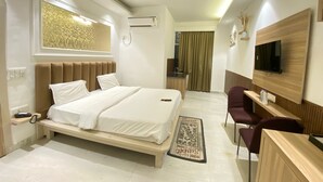A modern hotel room with a bed, desk, chair, TV, and a small kitchenette. - Hotel Elite One (Gurugram)