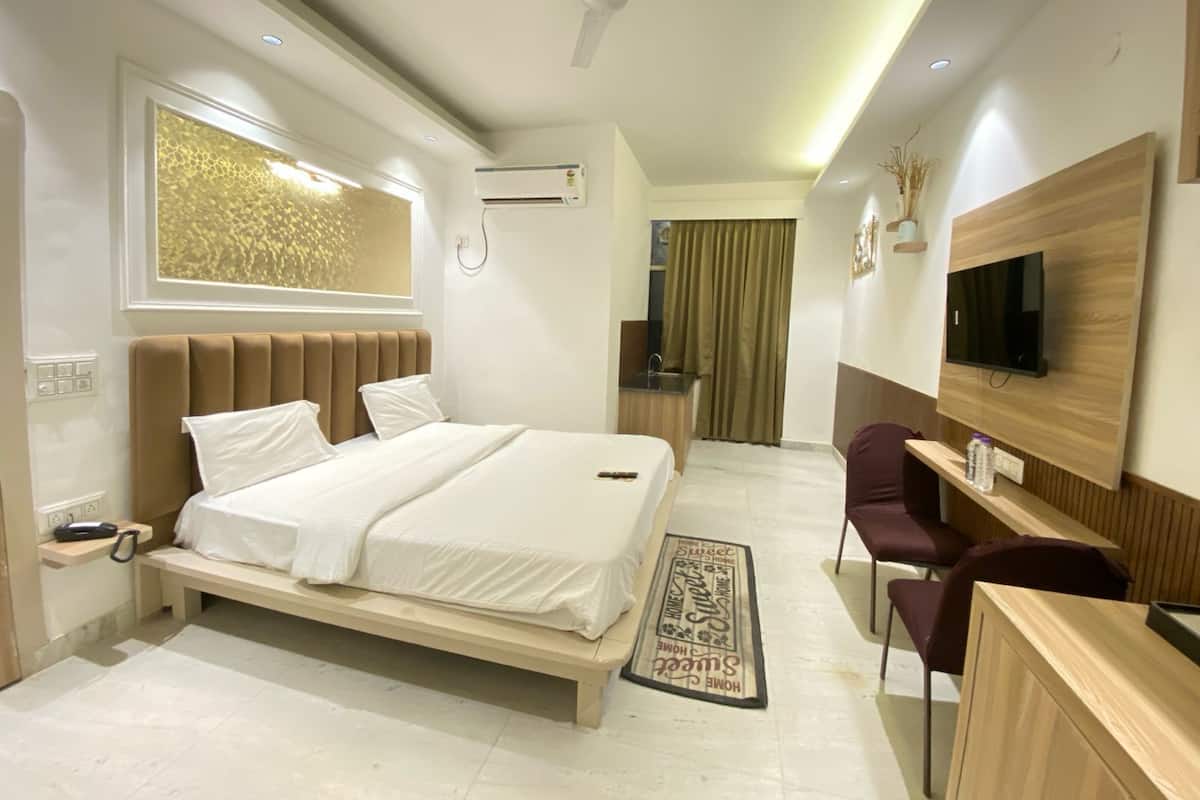 A modern hotel room with a bed, desk, chair, TV, and a small kitchenette.