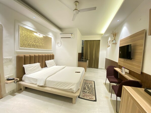 A modern hotel room with a bed, desk, chair, TV, and a small kitchenette.