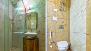 Un baño con ducha de vidrio, tocador de madera con lavamanos, espejo, inodoro y toallero en la pared.