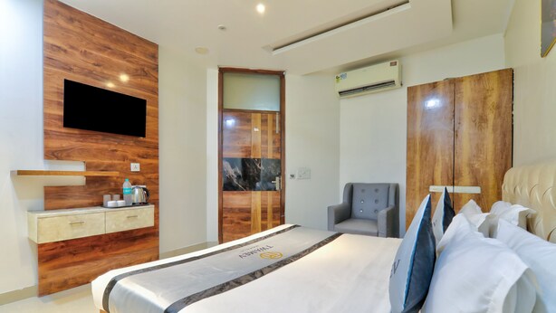 Habitación de hotel con cama, televisor montado en una pared de madera, escritorio con cafetera y una silla.