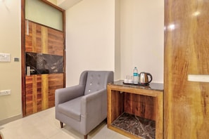 A room with a grey armchair, a wooden cabinet with a marble countertop, and a door with a wooden panel design. - Hotel Twamev Peeragarhi (New Delhi)