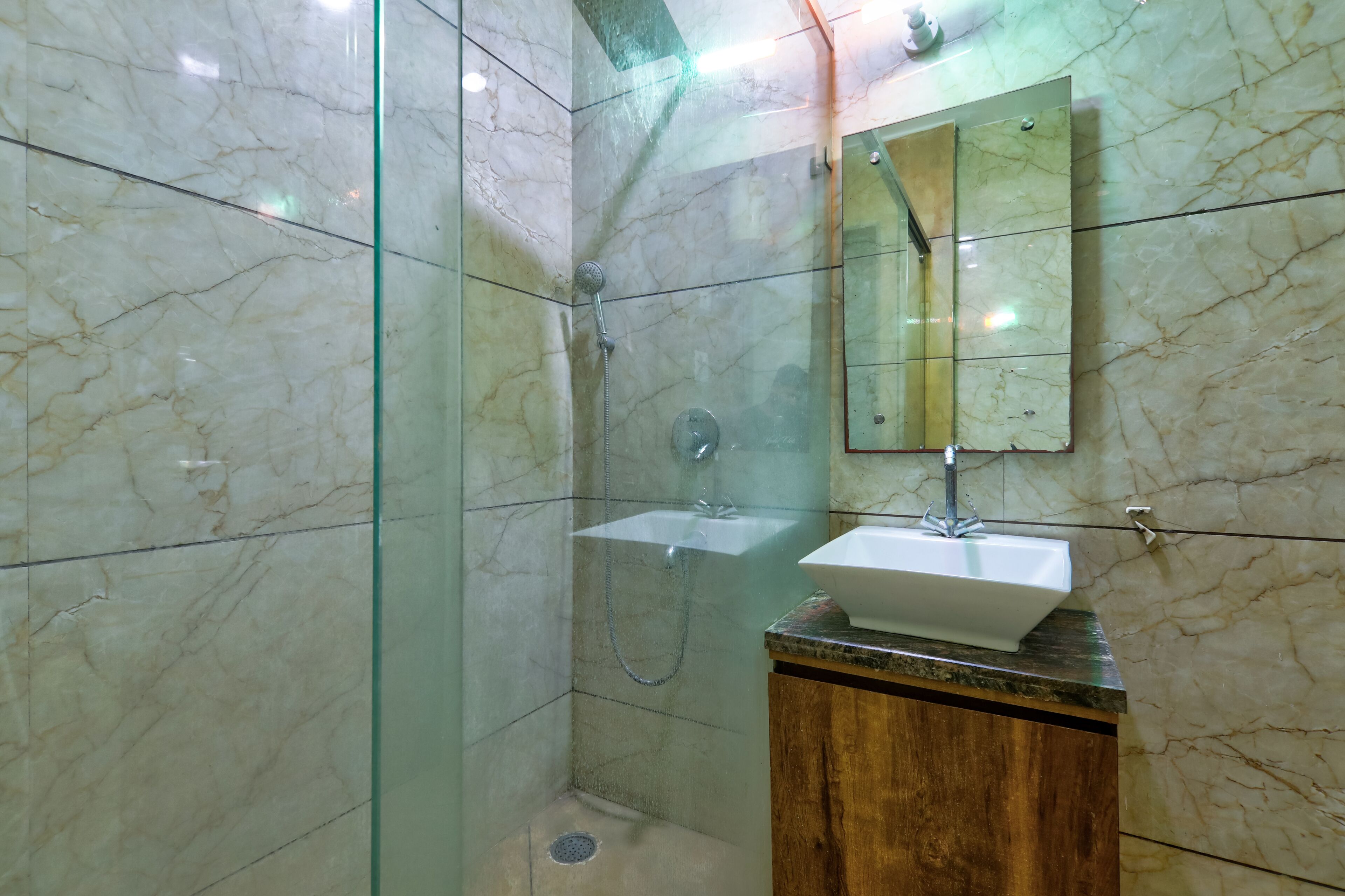 A bathroom with a glass-enclosed shower, a wooden vanity, and a marble-tiled wall.