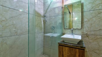 A bathroom with a glass-enclosed shower, a wooden vanity, and a marble-tiled wall.