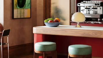 Una cocina con barra, taburetes, una cafetera y un frutero.