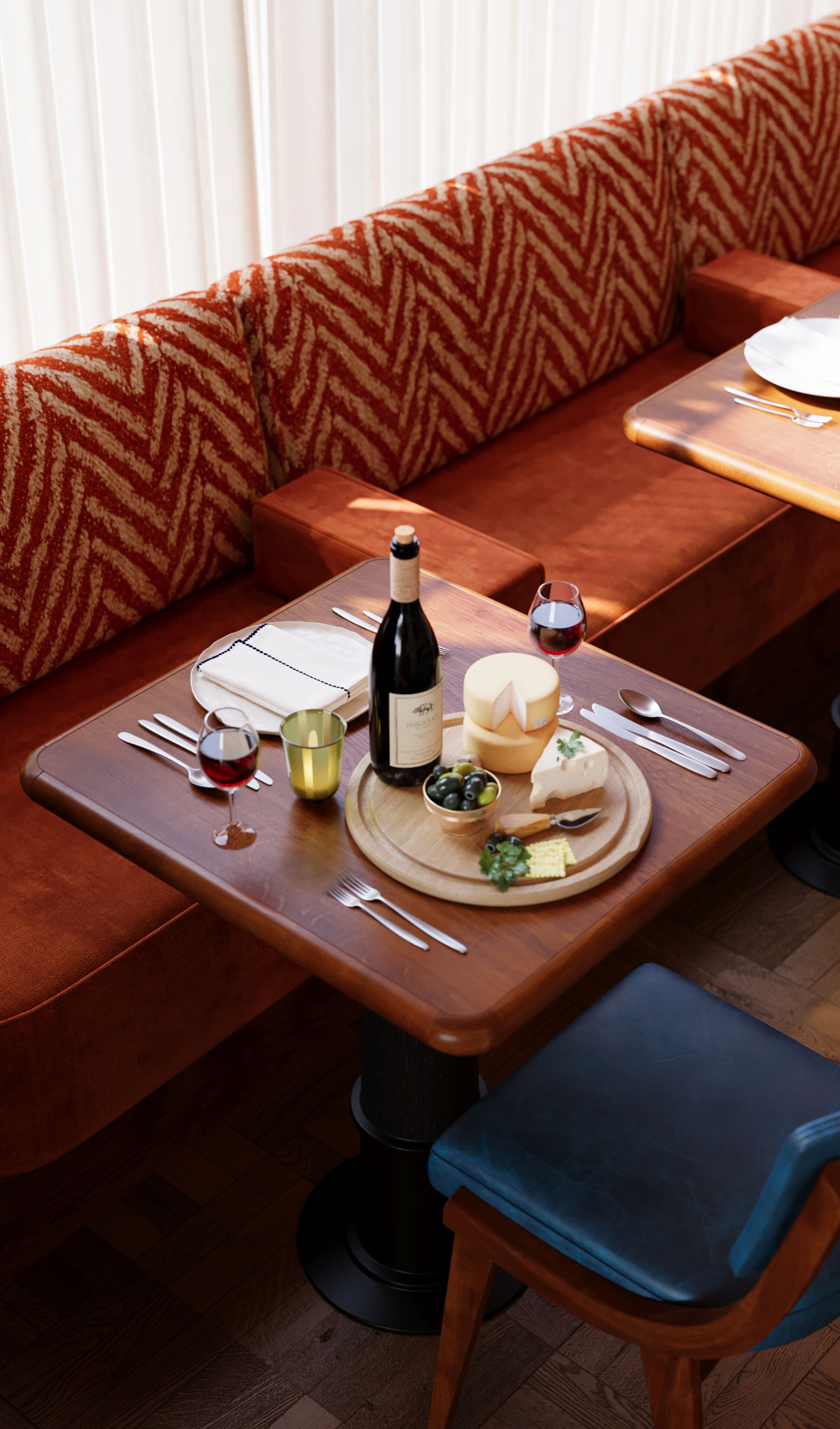 Un área de comedor con una mesa lista para dos personas, que incluye una botella de vino, queso, aceitunas y una copa de vino tinto.