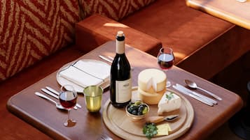 Un área de comedor con una mesa lista para dos personas, que incluye una botella de vino, queso, aceitunas y una copa de vino tinto.