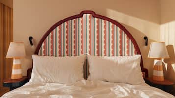 Una cama con ropa blanca, un cabecero a rayas y dos lámparas de noche.