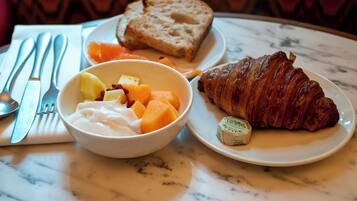 A breakfast setting with a croissant, butter, fruit, and yogurt on a marble table.