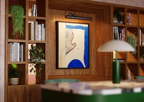 Una habitación con una estantería de madera, un cuadro abstracto enmarco y una lámpara verde.