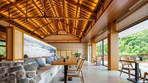 A spacious dining area with a long wooden table and chairs, a stone wall, and a large window with a view of greenery. - YAOJIA YANGXIN RESORT (Shaoxing)