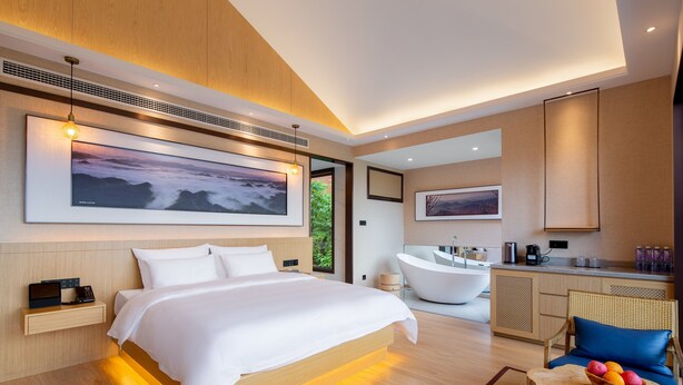 A modern hotel room with a large bed, a sitting area with a table and chairs, a bathtub, and a kitchen area. - YAOJIA YANGXIN RESORT (Shaoxing)