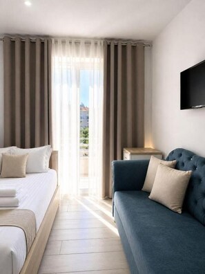 Habitación de hotel con cama, sofá, televisión montada en la pared y vistas por la ventana.