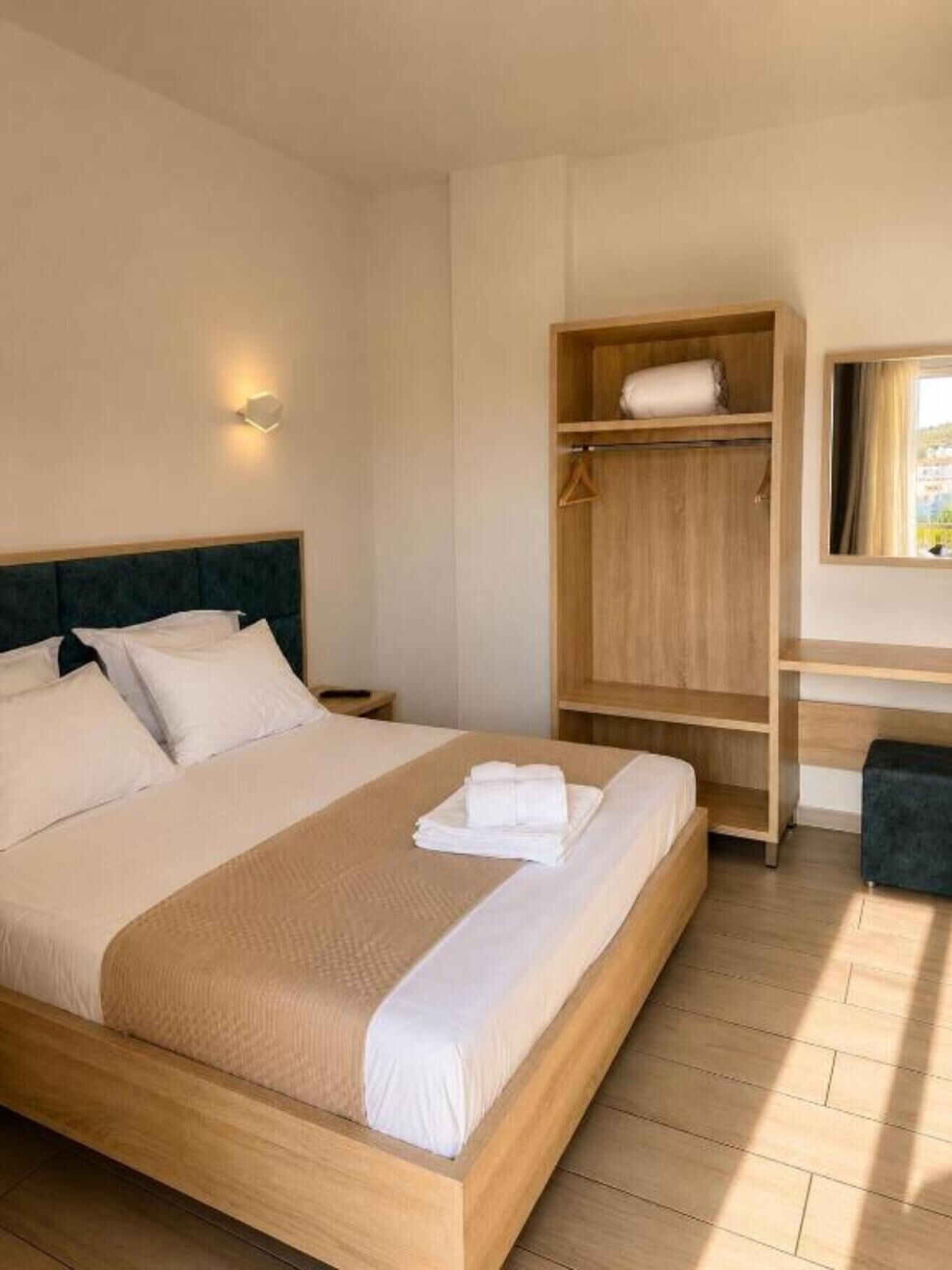 Een hotelkamer met een bed, een houten garderobe, een bureau met stoel en een raam.