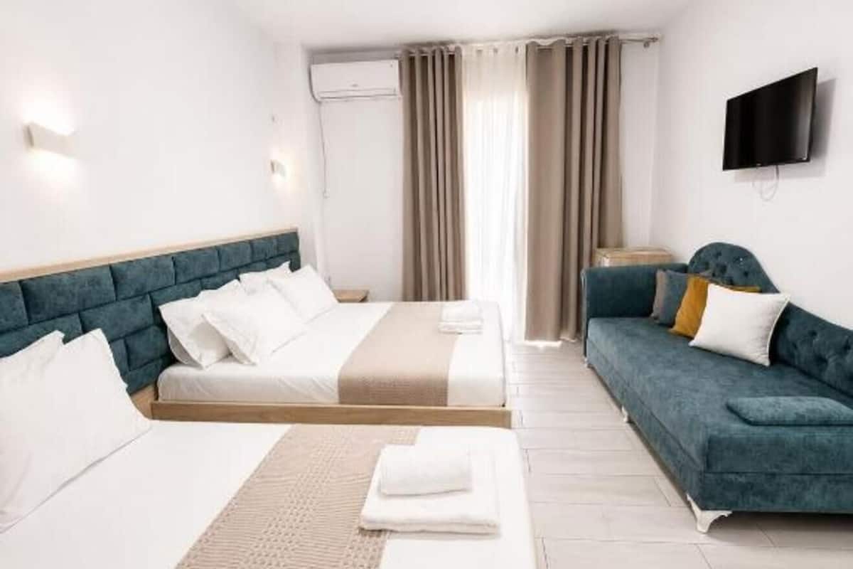 Habitación de hotel con dos camas, un sofá, un televisor de pantalla plana y un aire acondicionado.