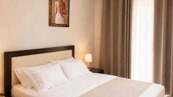 Un lit bien fait, avec du linge de lit blanc, une tête de lit et une table de chevet sur laquelle se trouve une lampe.