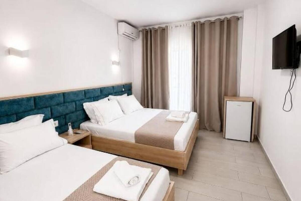 Habitación de hotel con dos camas, televisión, un refrigerador pequeño y aire acondicionado.
