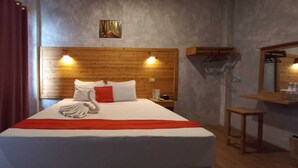 Ein Hotelzimmer mit hölzernem Kopfteil, einem Bett mit weißer und roter Bettwäsche, einer roten Tagesdecke, einem Nachttisch aus Holz, einem Spiegel und einer Holzablage.