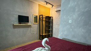 Ein Hotelzimmer mit Bett, Fernseher auf einem Regal, Spiegel, Bücherregal und Klimaanlage.
