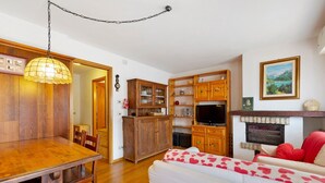 Uma área de refeições com uma mesa e cadeiras de madeira, um armário de madeira e uma televisão sobre um suporte.