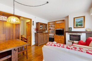 A dining area with a wooden table and chairs, a wooden cabinet, and a television on a stand. - Apartment 'Casa Fiori a Vinigo' with Mountain View and Balcony (Vinigo)