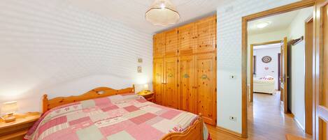 A bedroom with a wooden bed, a wooden wardrobe, and a ceiling light fixture.