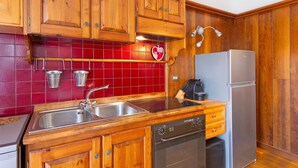Uma cozinha com armários de madeira, pia de aço inoxidável, lava-louças e geladeira.