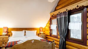 Une chambre à coucher située dans un chalet en rondins de bois, avec un lit, des tables de chevet et une fenêtre avec des rideaux.