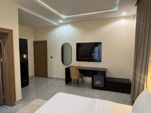 A modern hotel room with a bed, a desk with a chair, a television, and a mirror. - SUAVE BY CHLOE (Abuja)