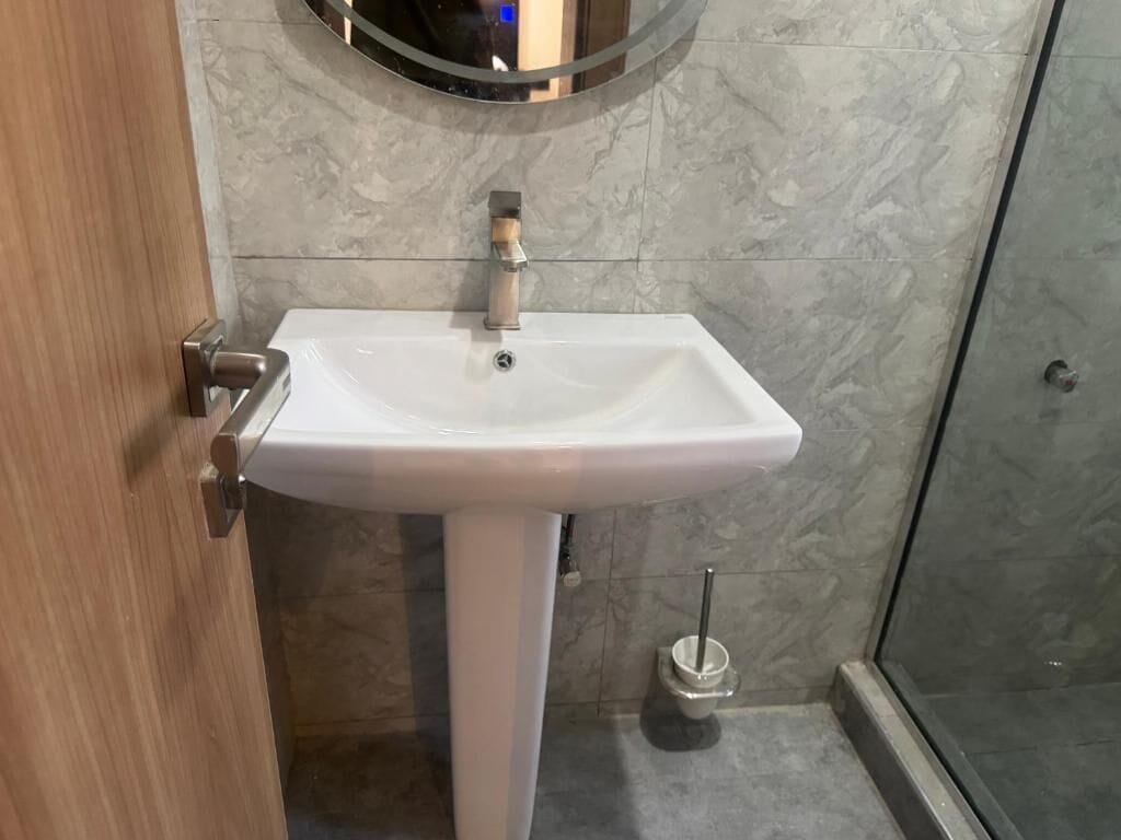 A bathroom with a white pedestal sink, a round mirror, and a toilet with a bidet attachment.
