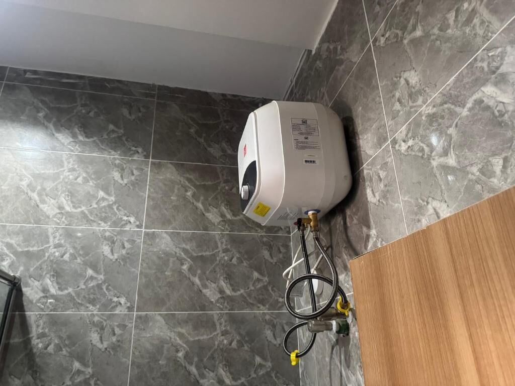 A water heater mounted on a tiled wall with a wooden cabinet below.