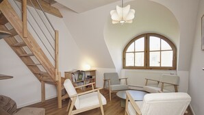 Een loft-achtige kamer met een houten trap, een ronde tafel en twee fauteuils.