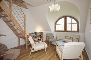 A loft-style room with a wooden staircase, a round table, and two armchairs. - Modern and comfortable vacation home - Reethaus Wiek right half of the house (Wiek)