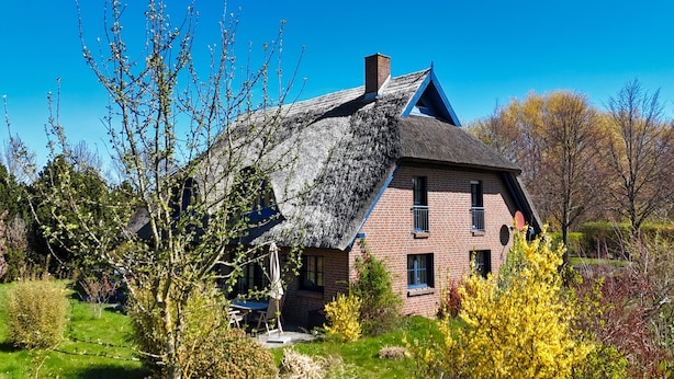 Een huis met rieten dak, bakstenen muren en een klein balkon.
