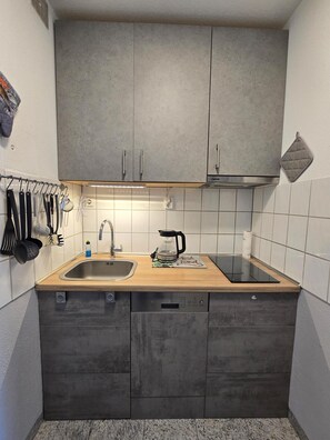 Eine kleine Küche mit einer Edelstahl-Spüle, einer Kaffeemaschine und einem Messerblock.