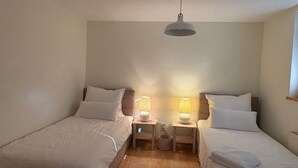 Ett rum med två sängar, en taklampa, sänglampor och ett trägolv.