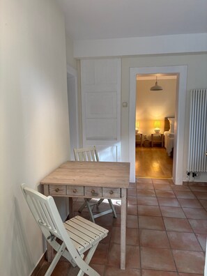 Un espace repas avec une table et des chaises en bois, une porte blanche et un sol carrelé.