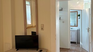 Ett rum med en byrå i trä, en platt-TV, en spegel och en dörr som leder till ett badrum.