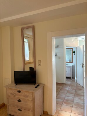 A room with a wooden dresser, a flat-screen TV, a mirror, and a door leading to a bathroom.