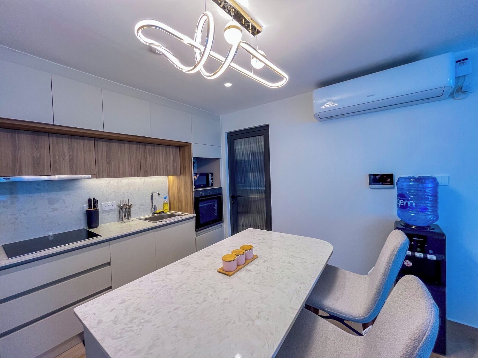 A modern kitchen with a marble countertop, built-in appliances, and a unique ceiling light fixture.