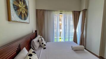 Una habitación de hotel con una cama grande, cabecera, una obra de arte colgada en la pared y vistas al exterior a través de cortinas traslúcidas.
