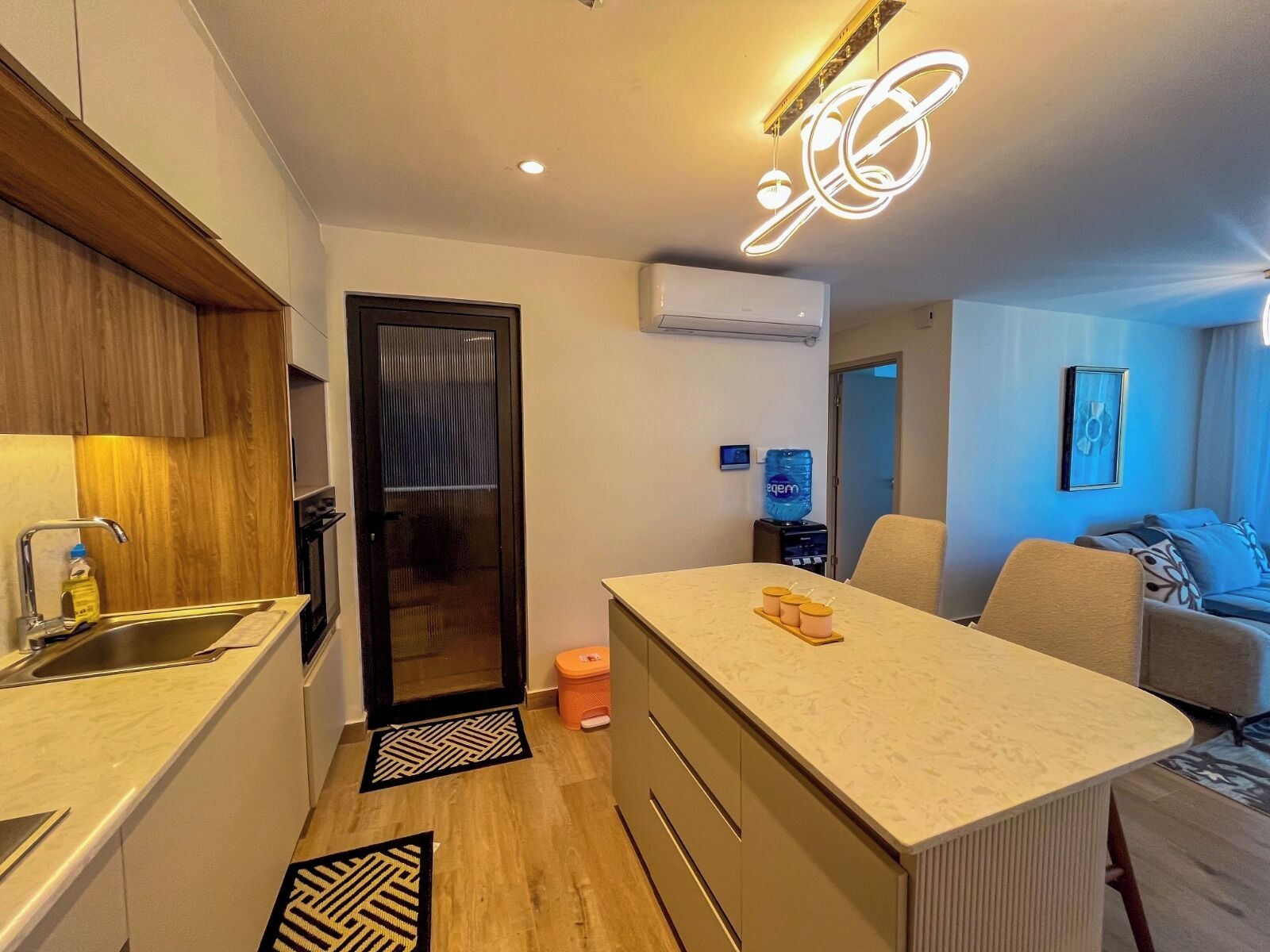 Uma cozinha moderna com ilha central, área de jantar com sofá e sala de estar com poltrona.